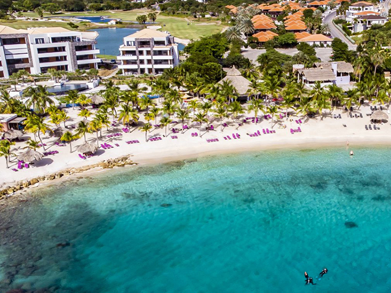 An aerial view of Bayside Beach Hotel in Curaçao showing the beach and divers swimming in clear water.