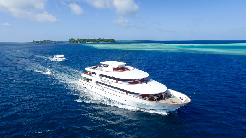 The Carpe Vita Explorer cruises past small islands that are typical of the Maldives. The ship's dive dhoni is following.
