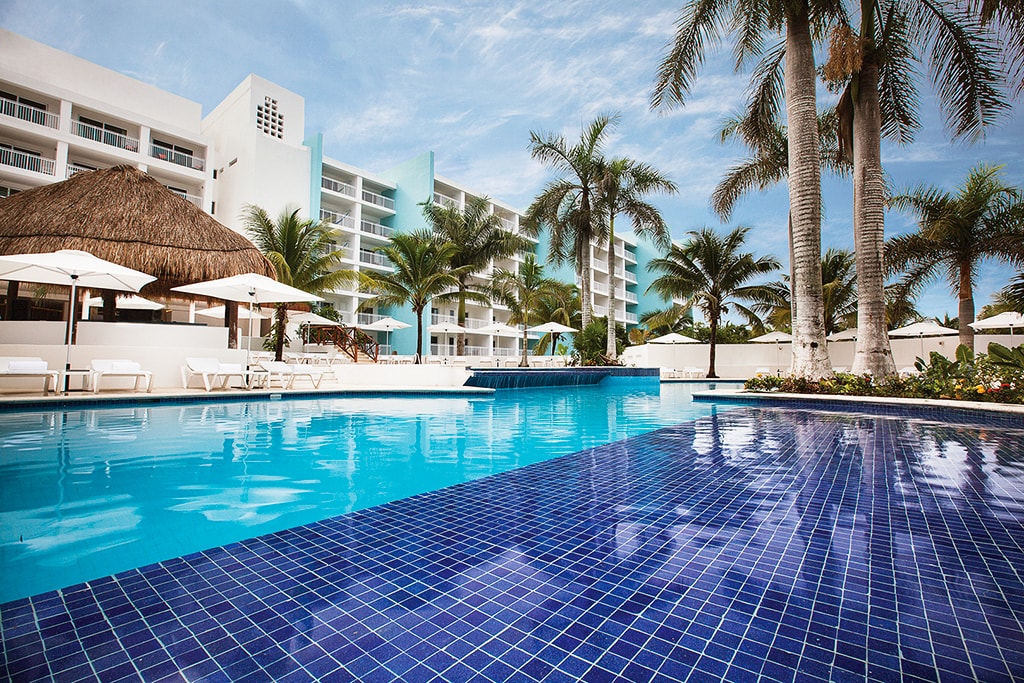 The pool is a focal point of daily social activities, with a swim-up bar and groups of lounges and day beds spaced around a landscaped deck.